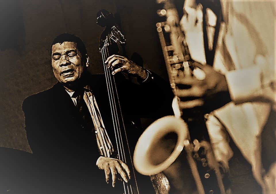 A sepia-toned photo of a bassist and a tenor saxophonist playing side by side.