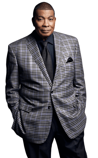 Kent Miller in a black-and-white checked sport coat, hands in his pockets, against a black background.