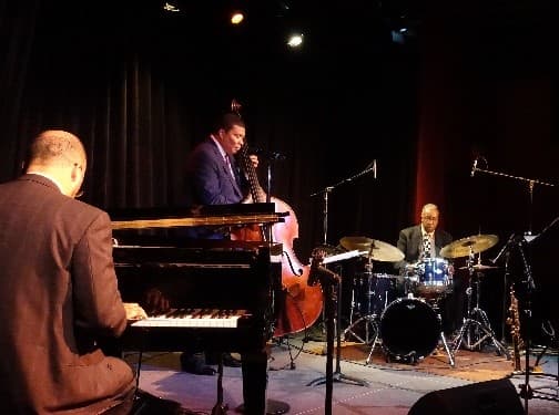 A jazz trio on stage, with the pianist in the foreground and a bassist and a drummer behind.